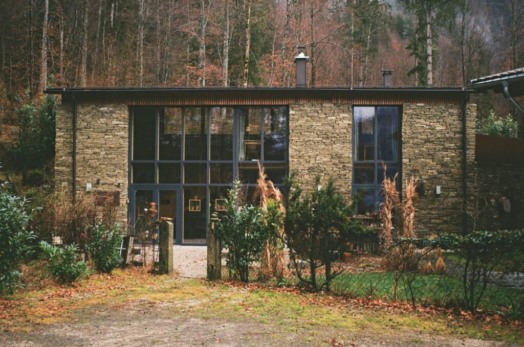 A forest house with two story windows and covered in dry stack stone siding