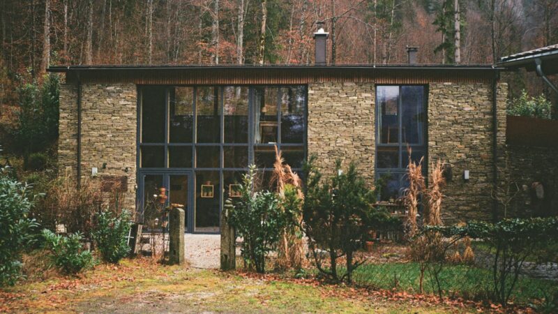 A forest house with two story windows and covered in dry stack stone siding